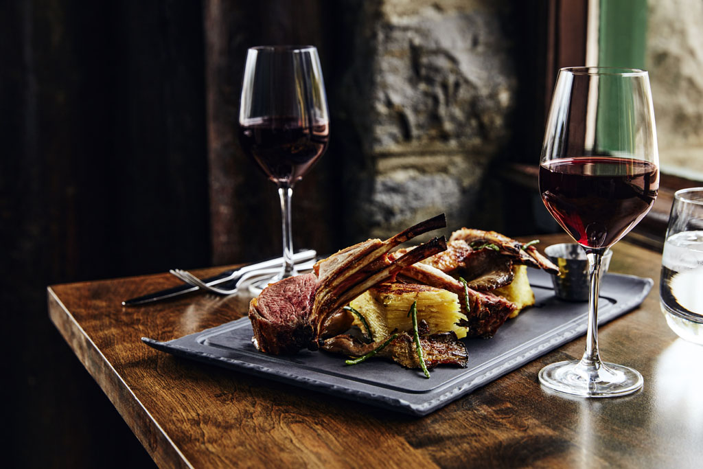 a plate of meat and potatoes with wine glasses on a table