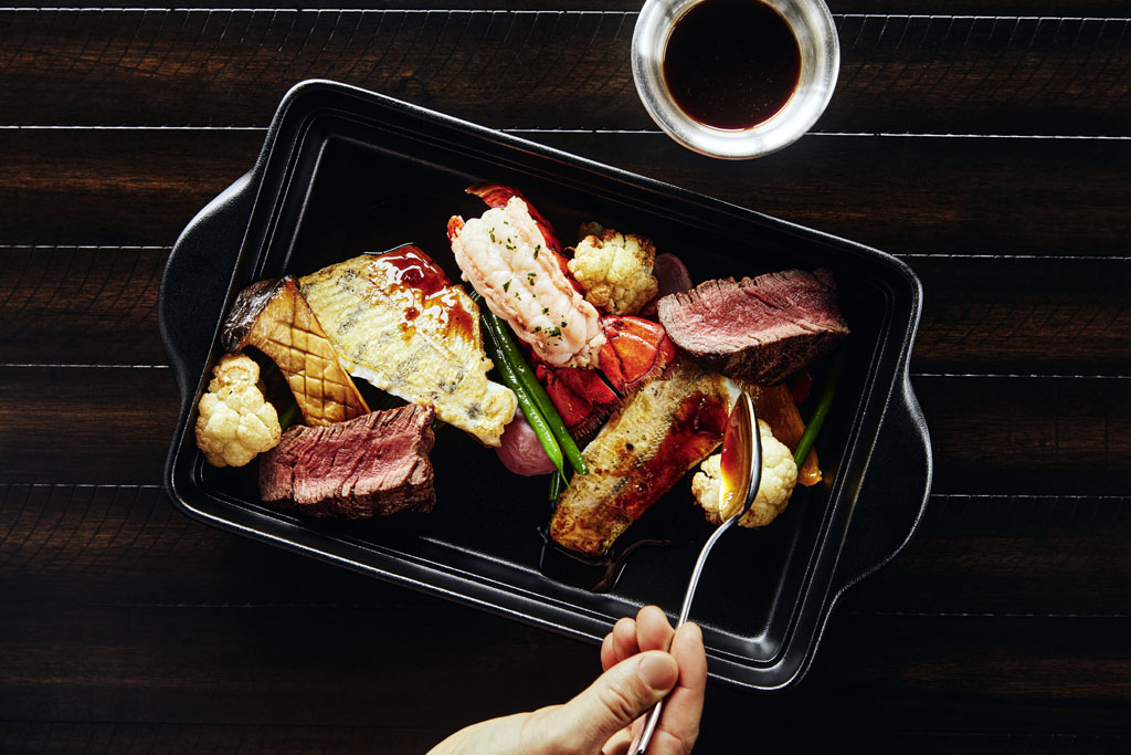 a person holding a spoon over a tray of food