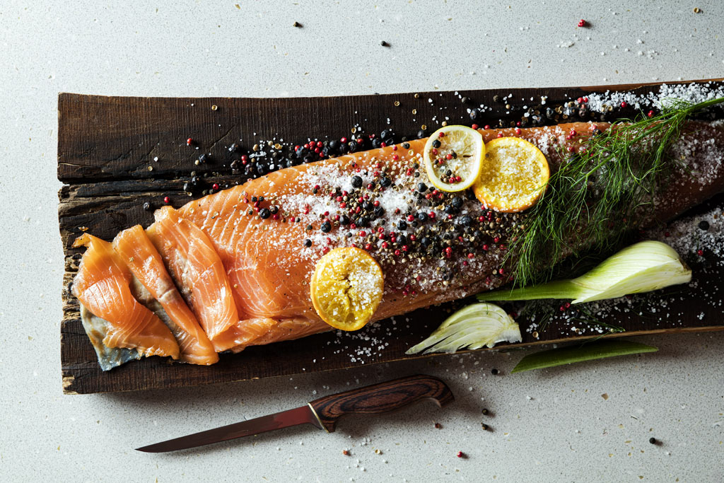 a piece of fish with spices and lemons on a wooden board