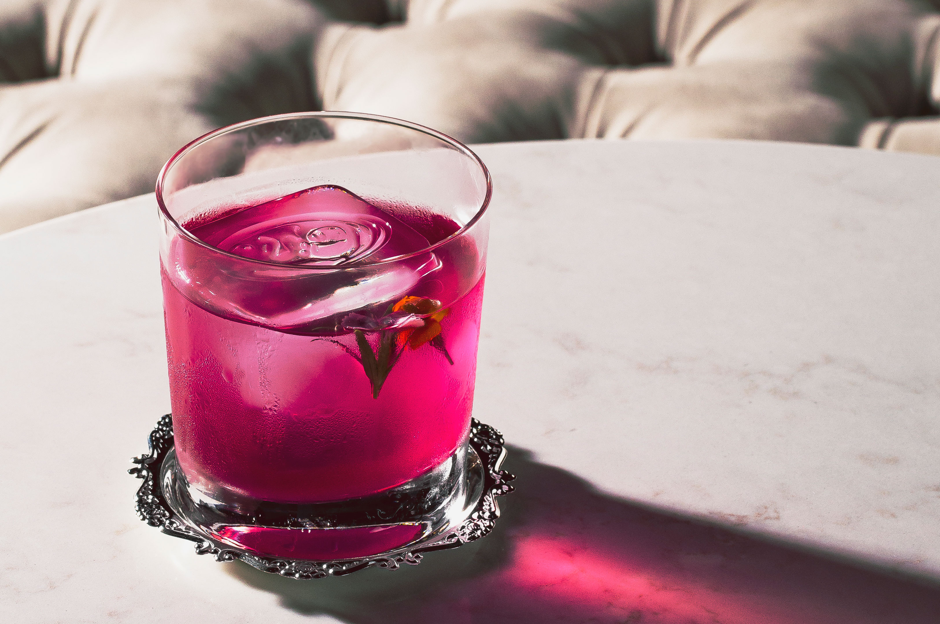 a glass with pink liquid and ice on a silver tray