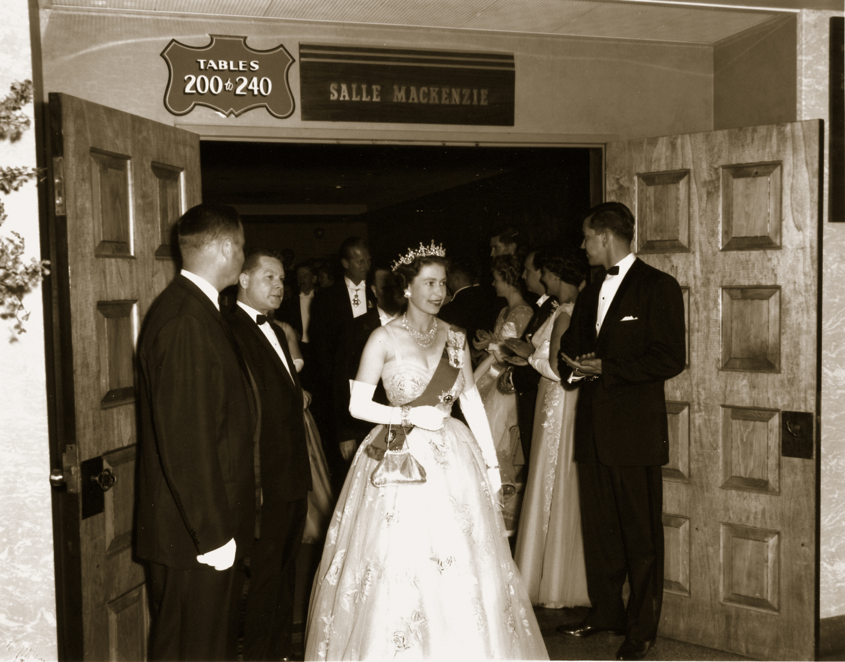 a woman in a dress and crown standing in front of a group of people