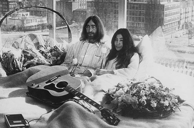 a man and woman sitting in bed with a guitar and flowers