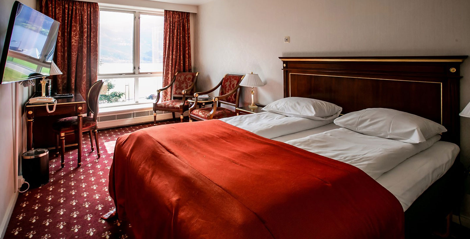 a bed with a red blanket and chairs in a room with a window