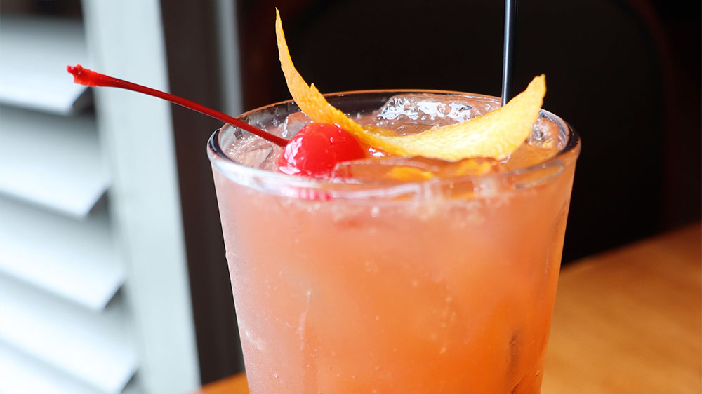 a drink with orange peels and a cherry in a glass