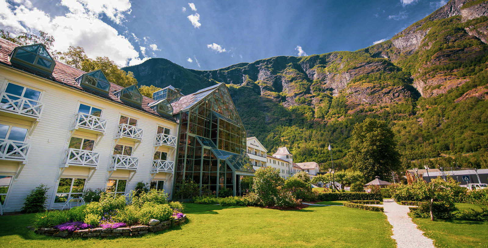 a building with a large glass roof and a green lawn with a mountain in the background