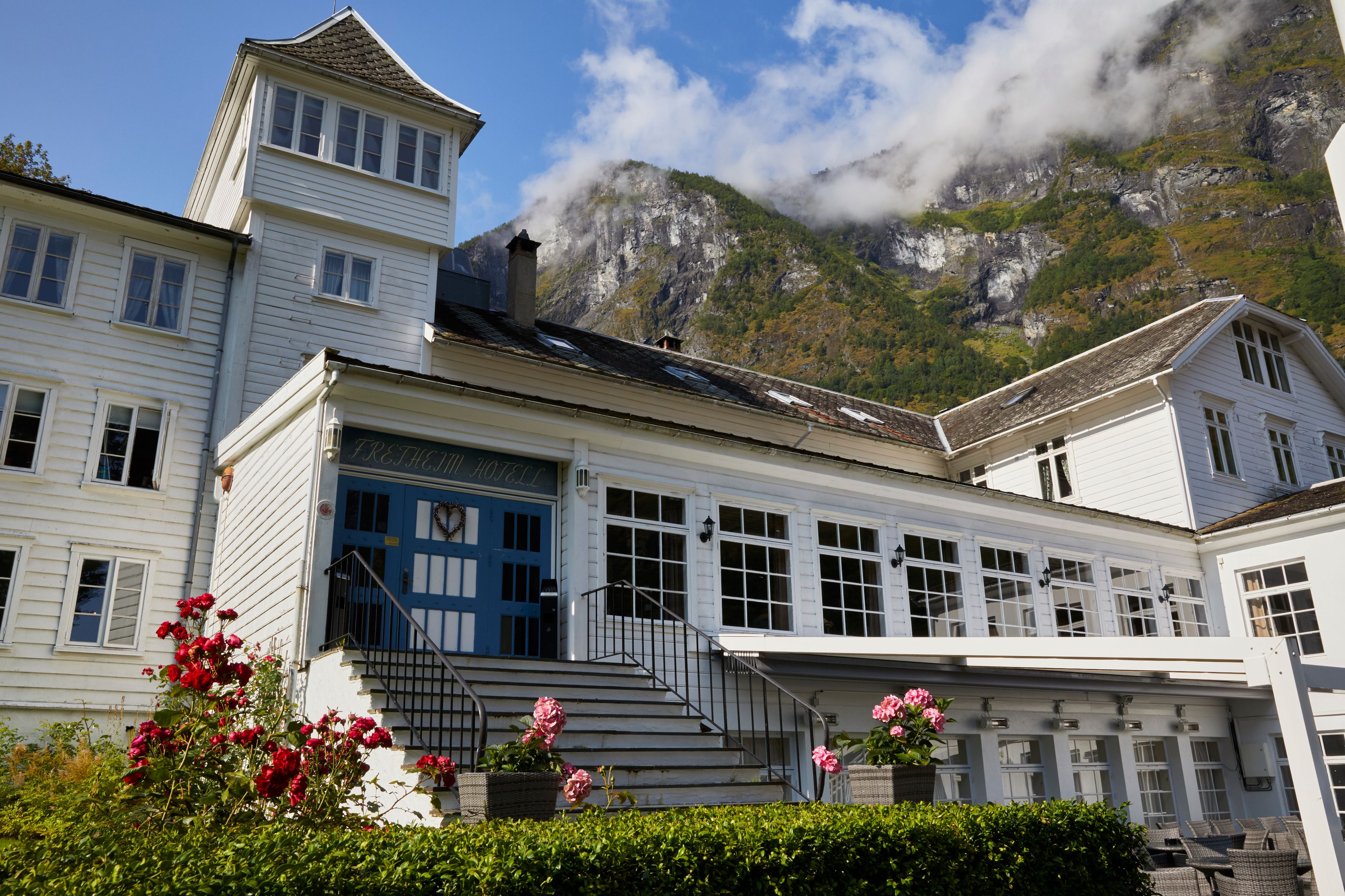 a white building with a blue door and stairs leading to a mountain