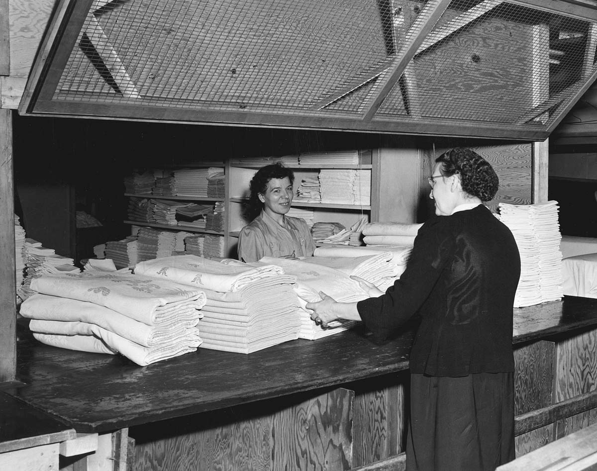 a woman handing a woman a stack of fabric