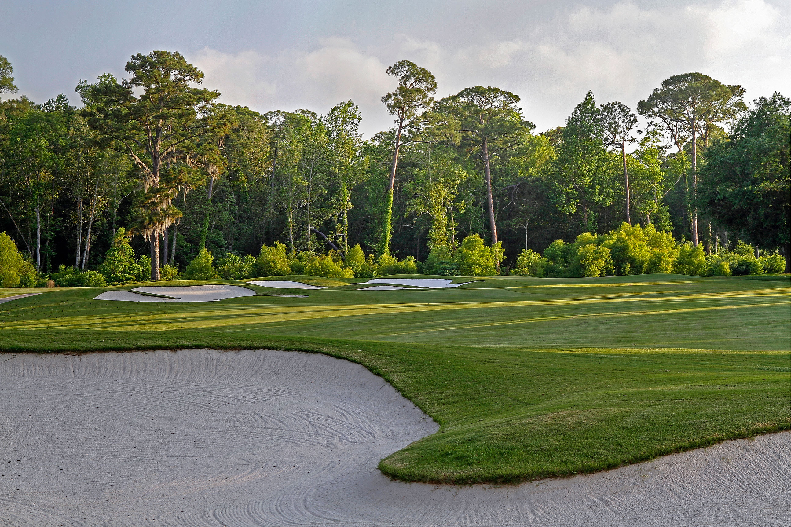 a golf course with sand bunkers and trees with Augusta National Golf Club in the background