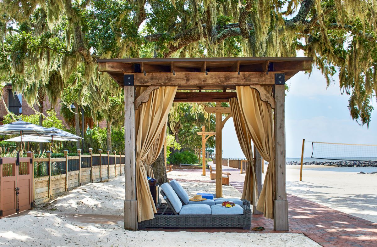 a wooden structure with a couch under a canopy with a beach and trees