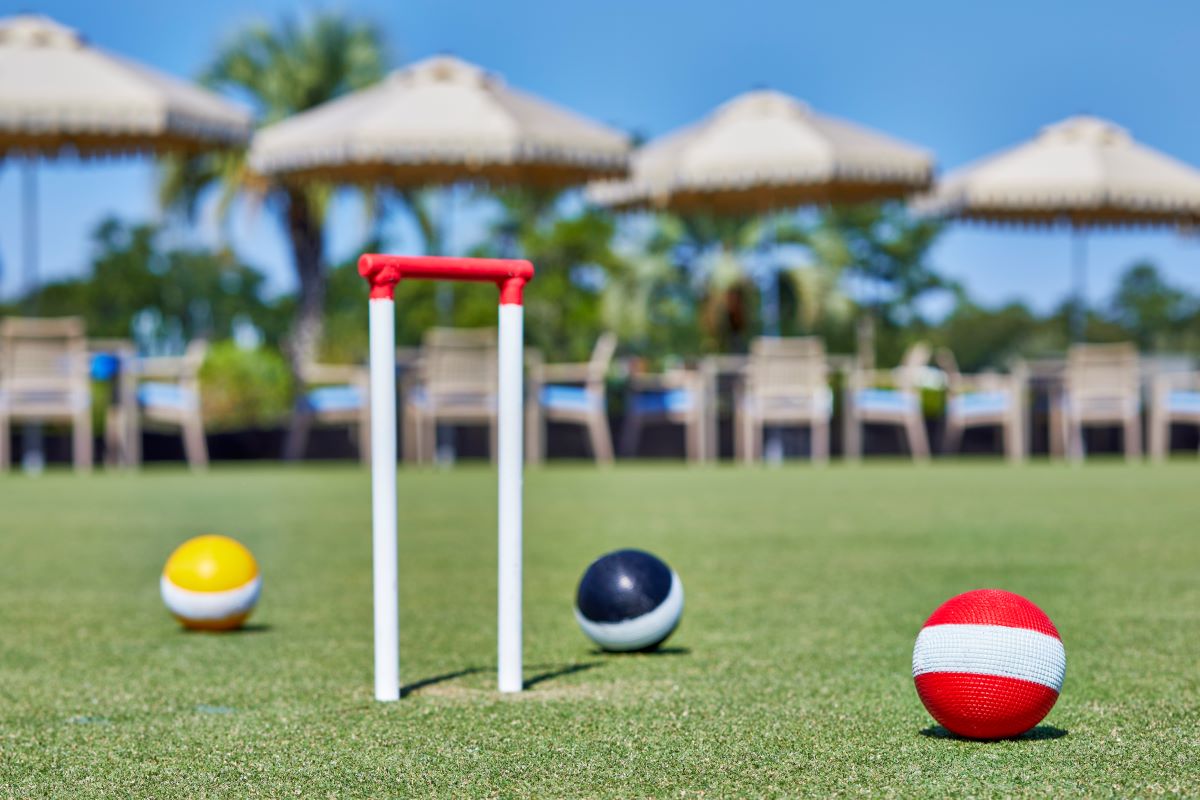 croquet balls on a grass field with umbrellas and chairs in the background