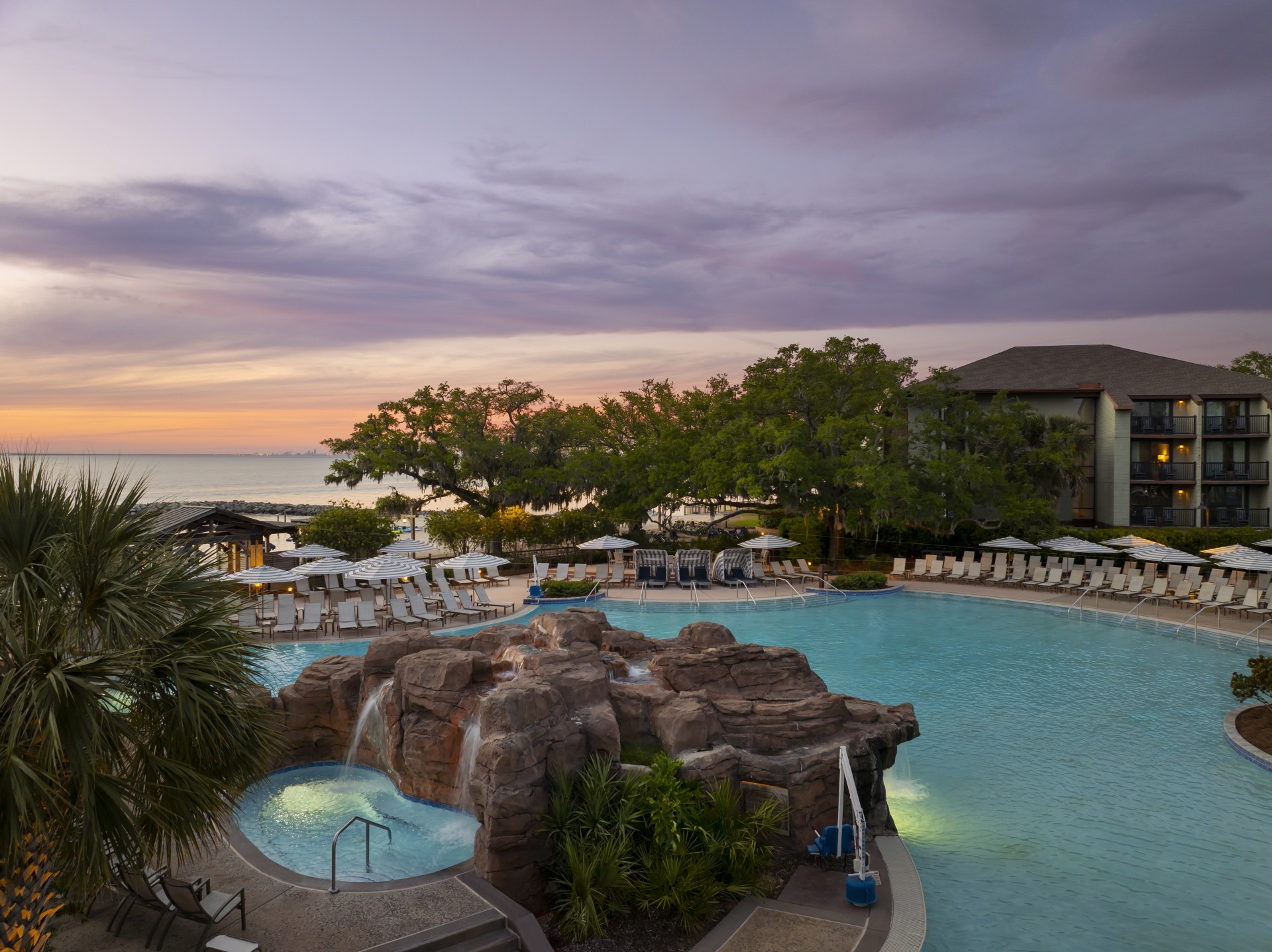 a pool with a waterfall and a rock fountain and a beach and trees