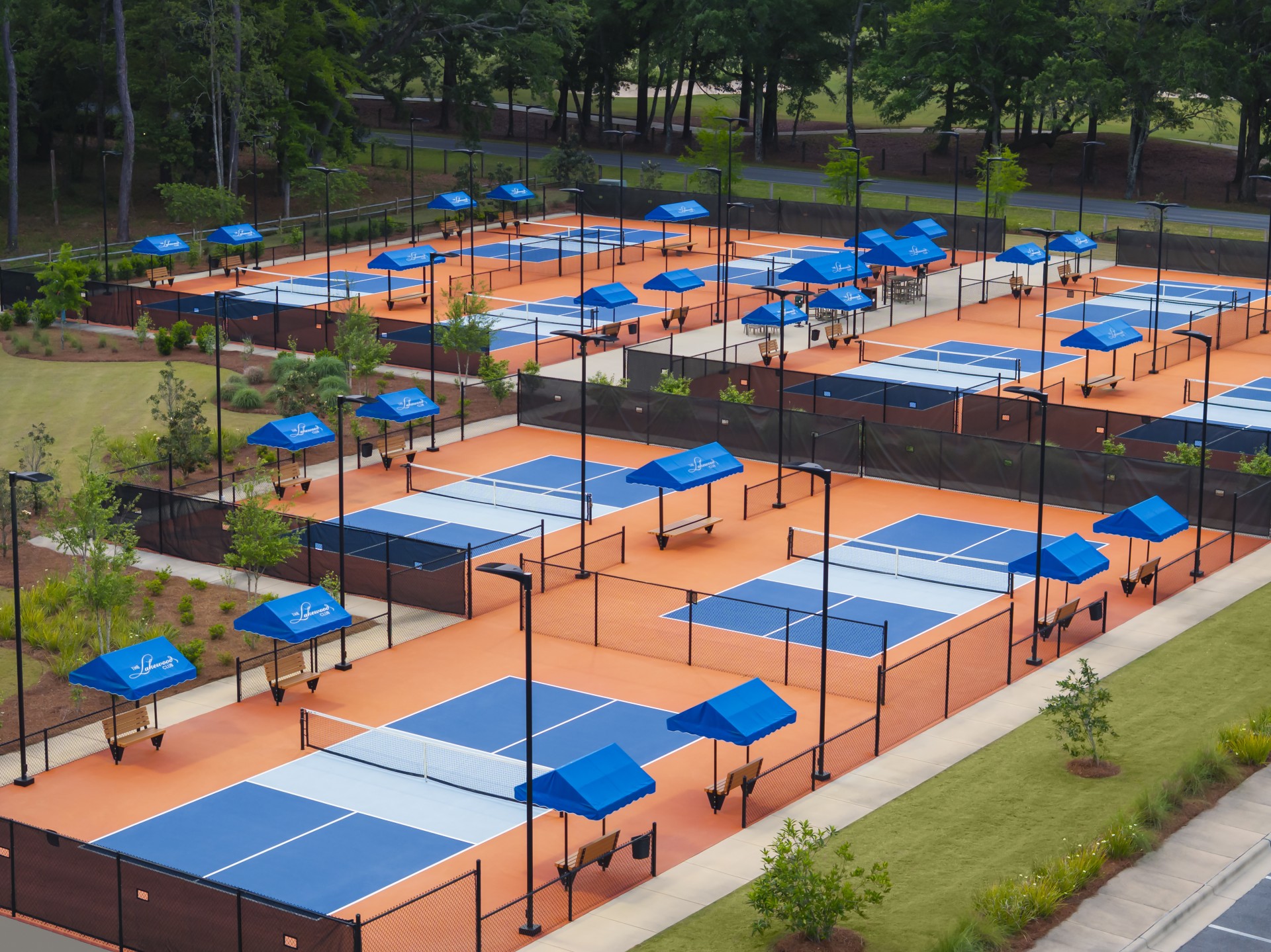 Aerial view of an outdoor pickleball facility featuring blue and orange courts equipped with shaded bench seating.