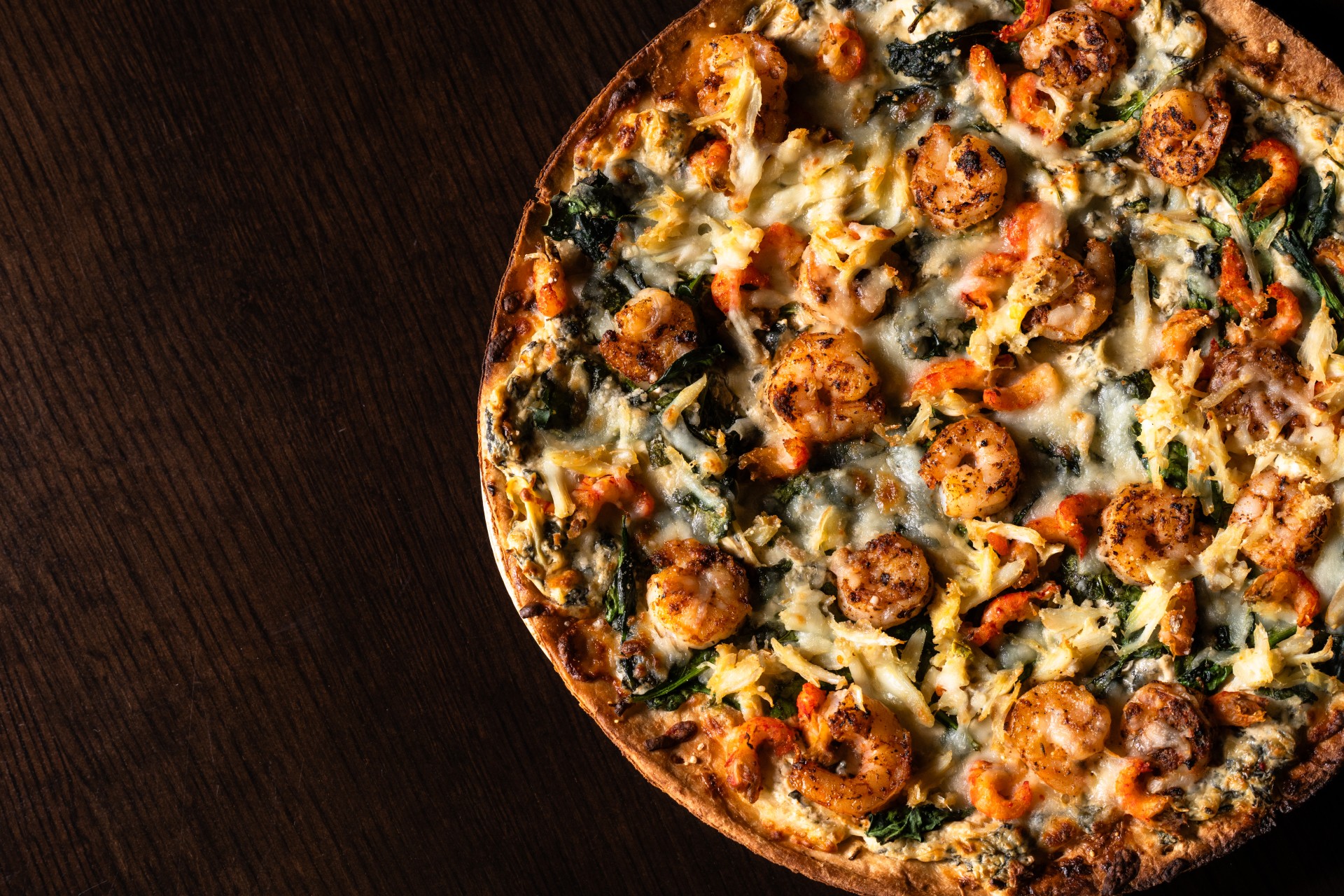 a pizza with shrimp and spinach on a wood surface