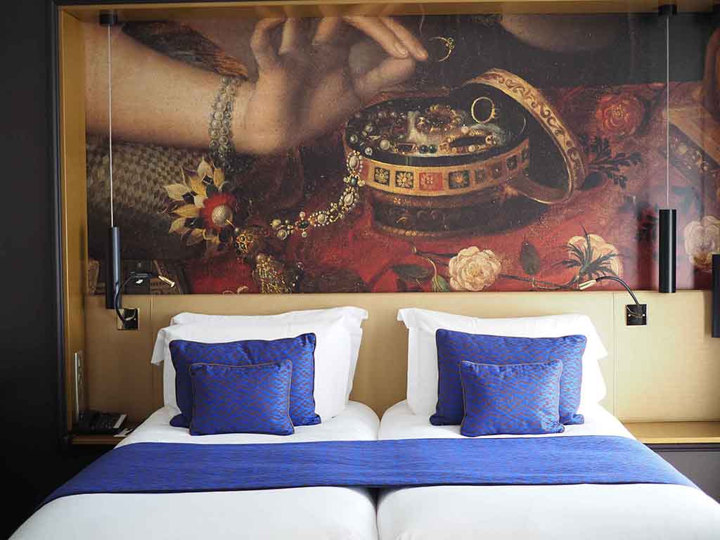 a bed with blue pillows and a painting on the wall