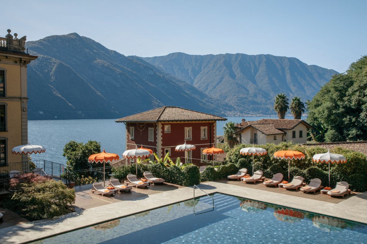a pool with chairs and umbrellas by a house and mountains