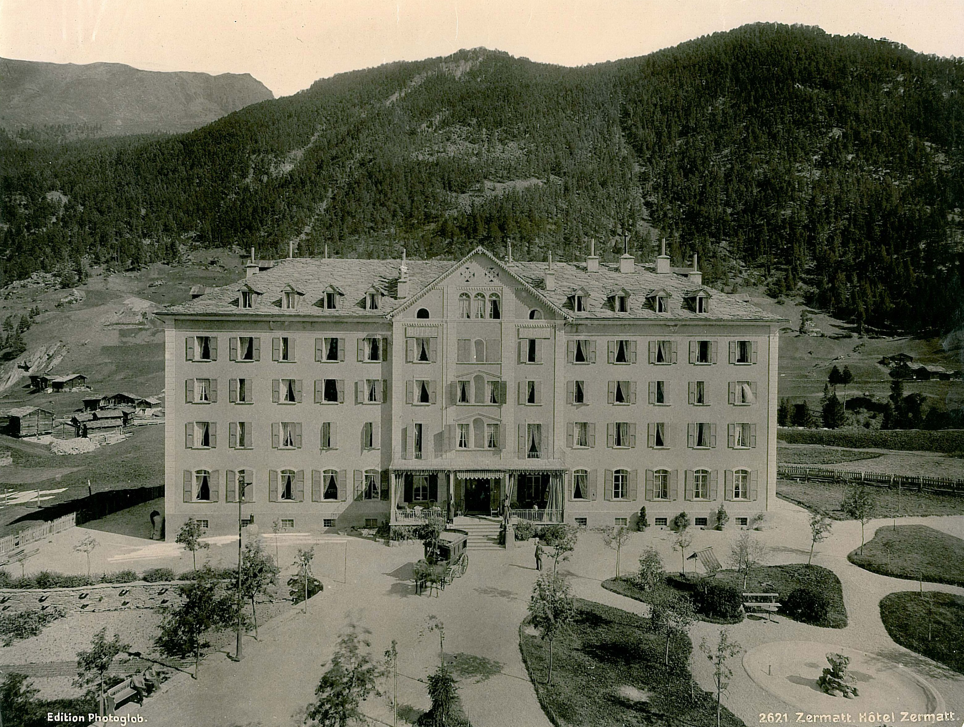 a large building with trees and mountains in the background