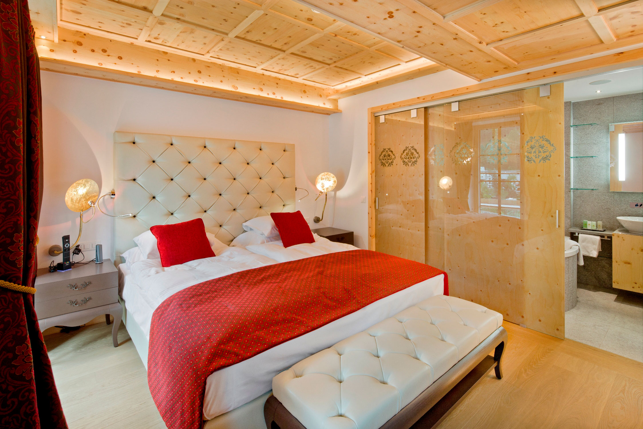 a bed with red pillows and a white bed with a glass door
