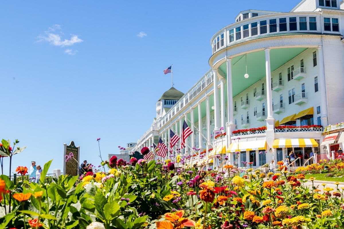 a large white building with a balcony and a flower garden with Grand Hotel in the background
