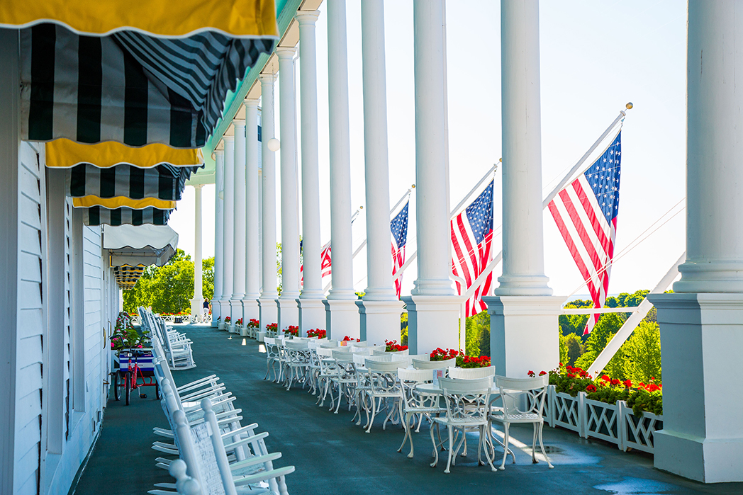a row of white chairs and tables with flags on a porch