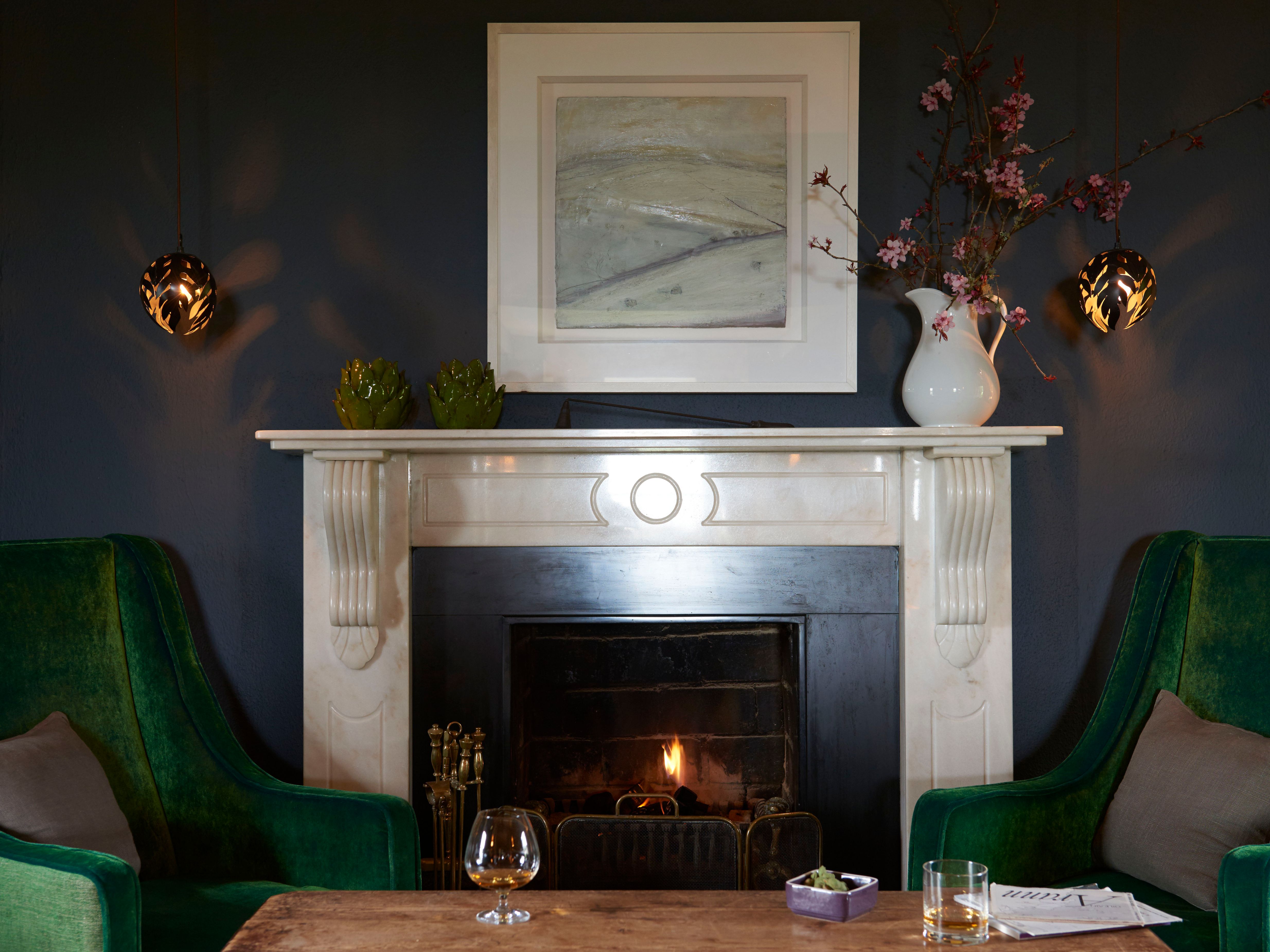 a fireplace with green chairs and a painting above it