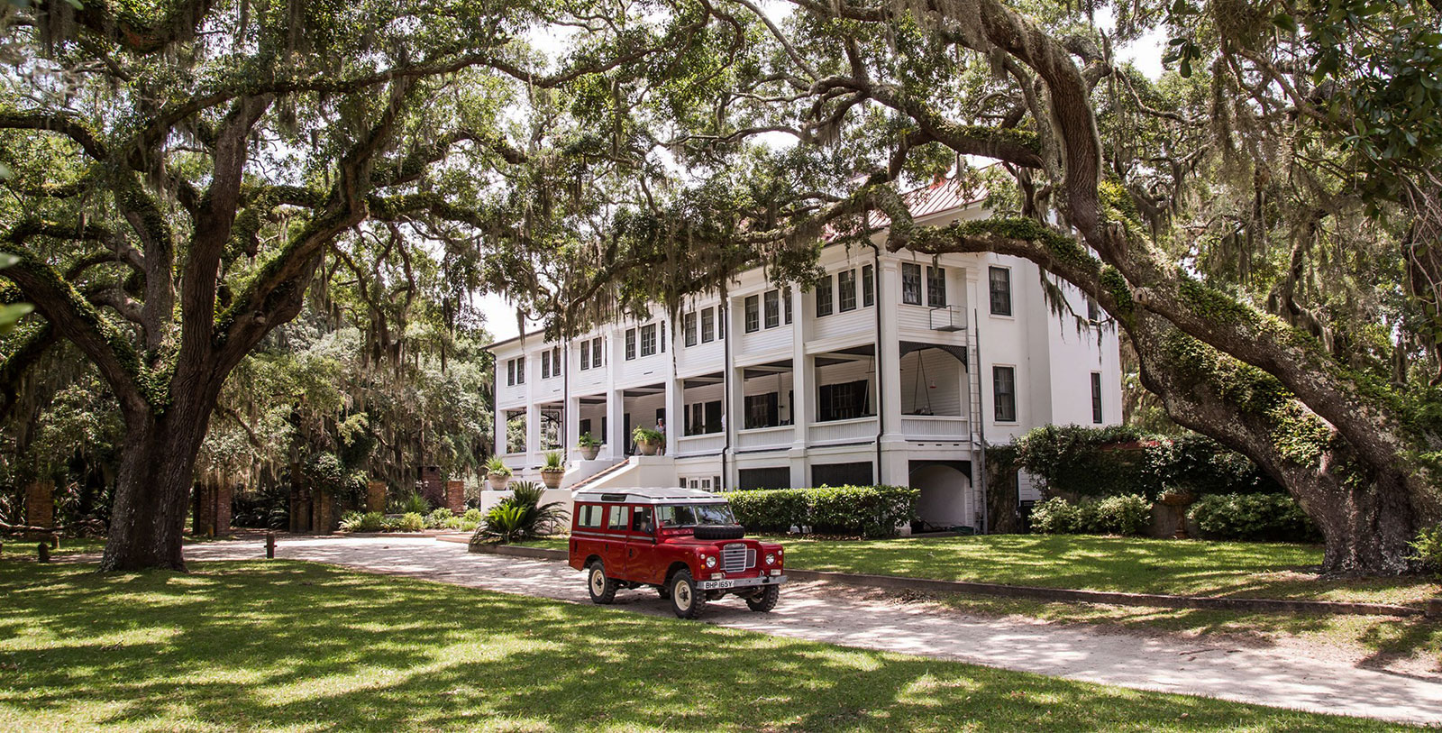 a red car parked in front of a large white building with Bragg-Mitchell Mansion in the background