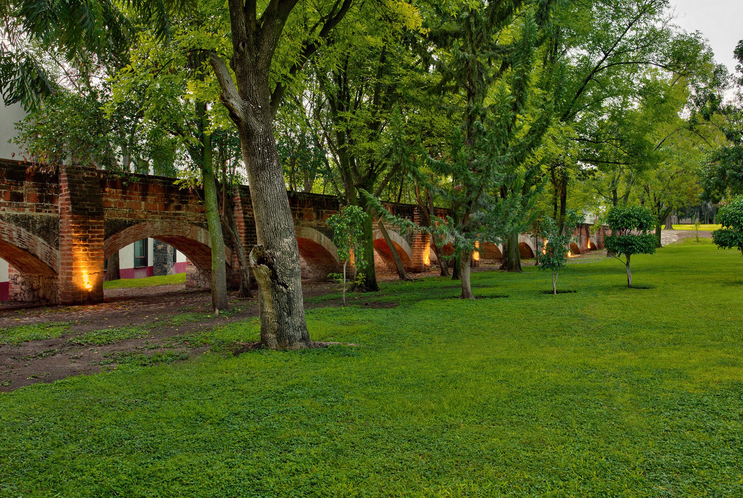 a grass field with trees and a brick bridge