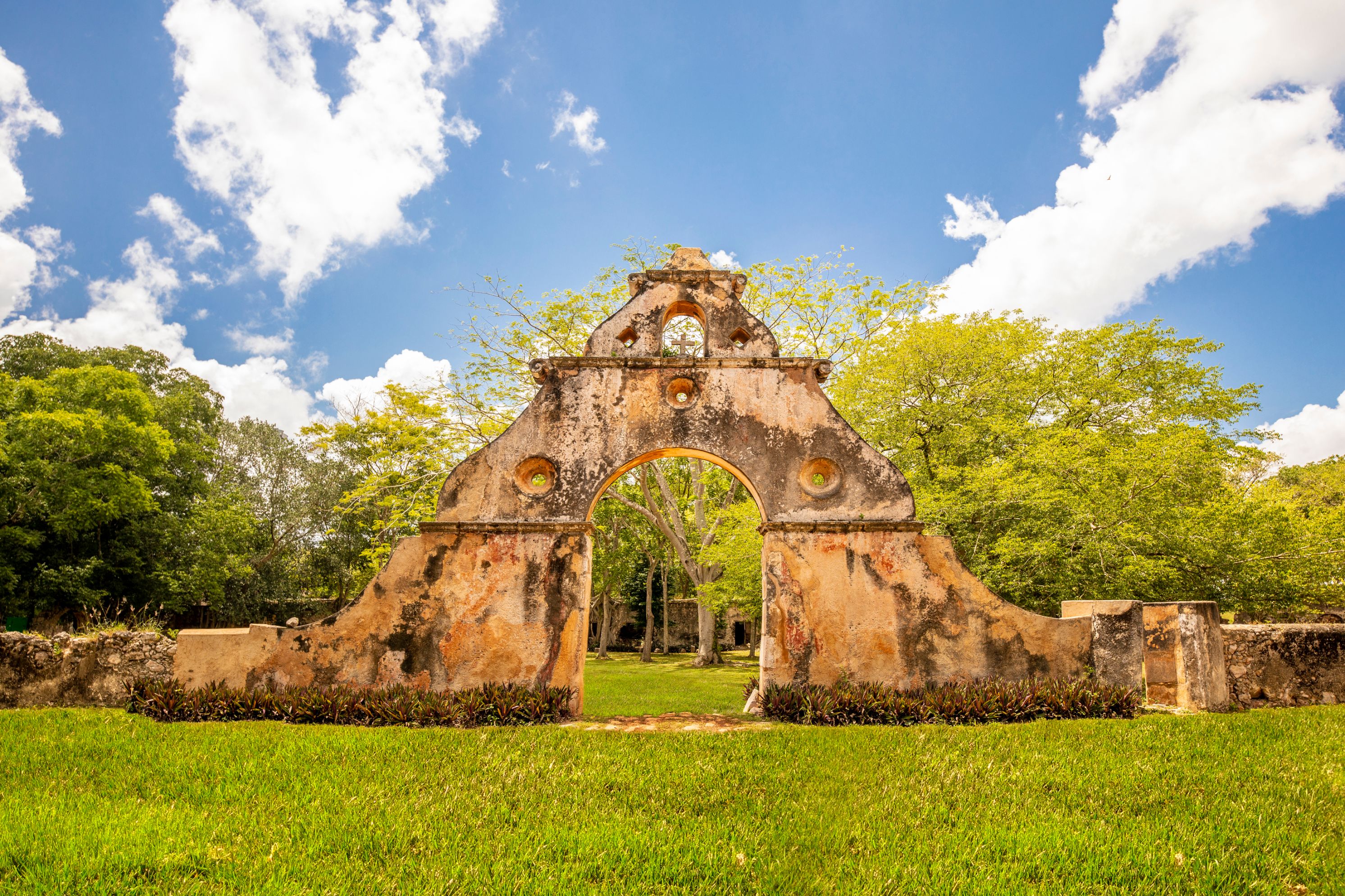 a stone arch with a green lawn and trees