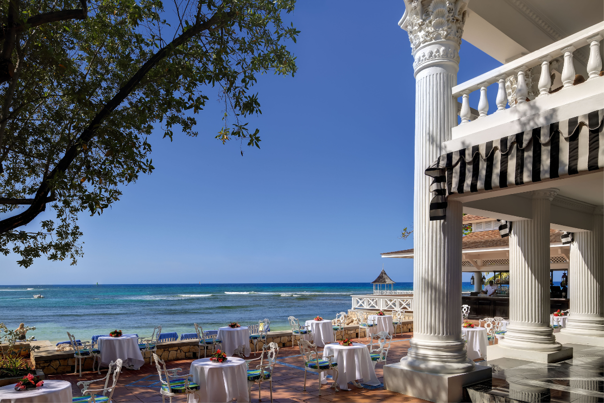 a white pillars with tables and chairs on a patio with a body of water