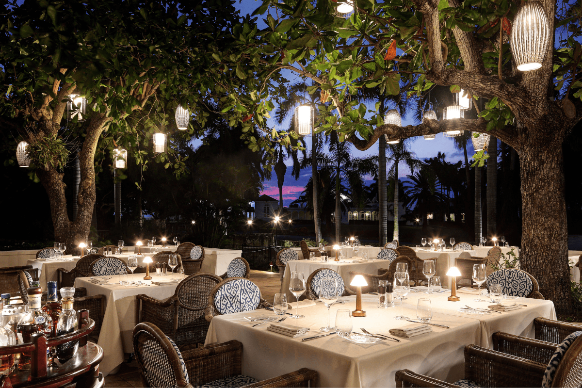tables outside tables with white tablecloths and plates with lights from trees
