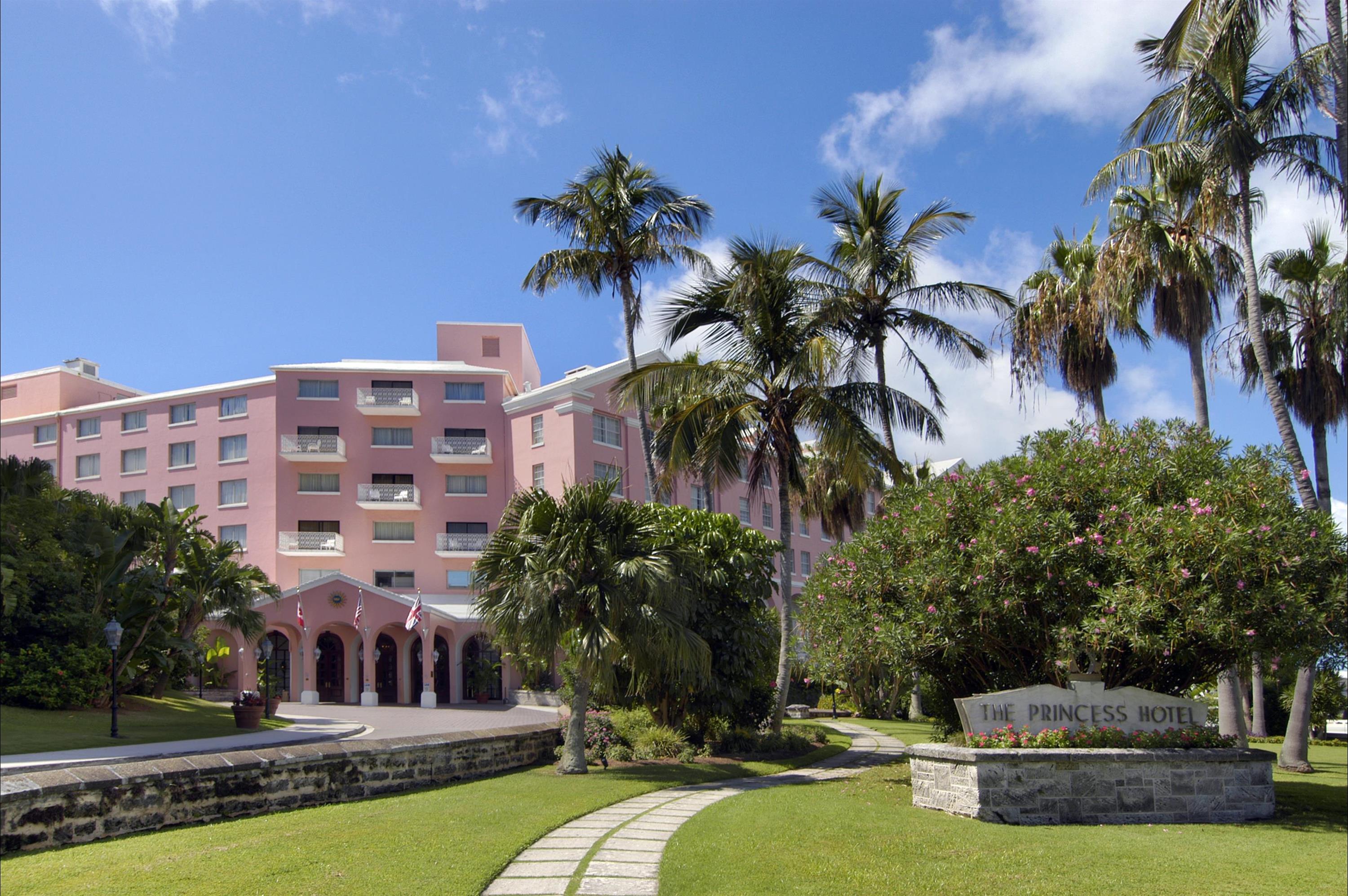 a pink building with palm trees and a sign