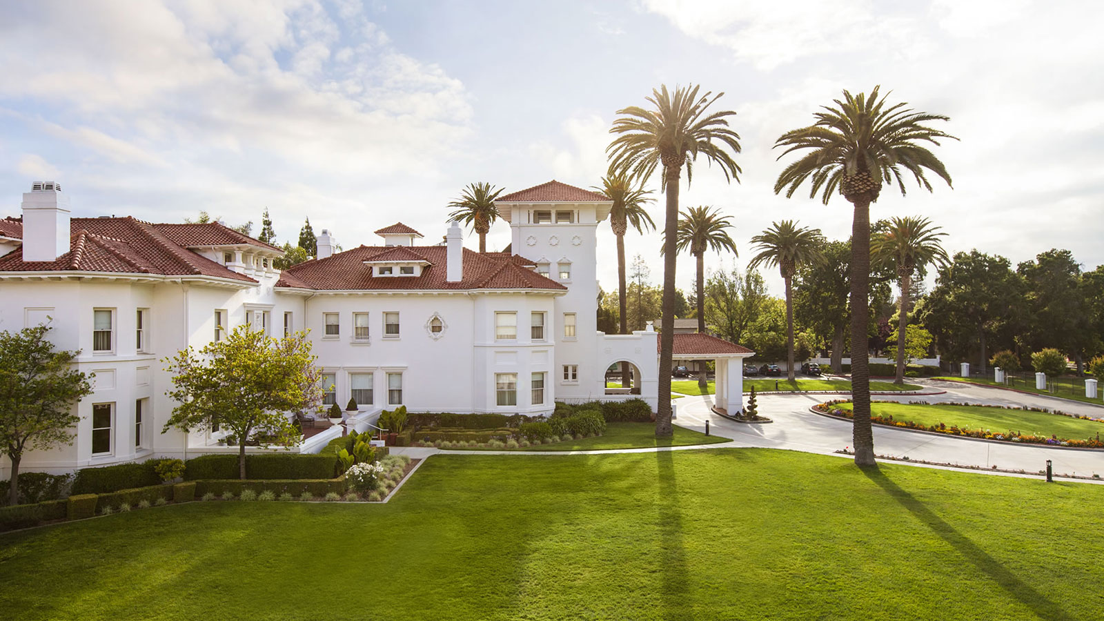 a large white building with a lawn and palm trees
