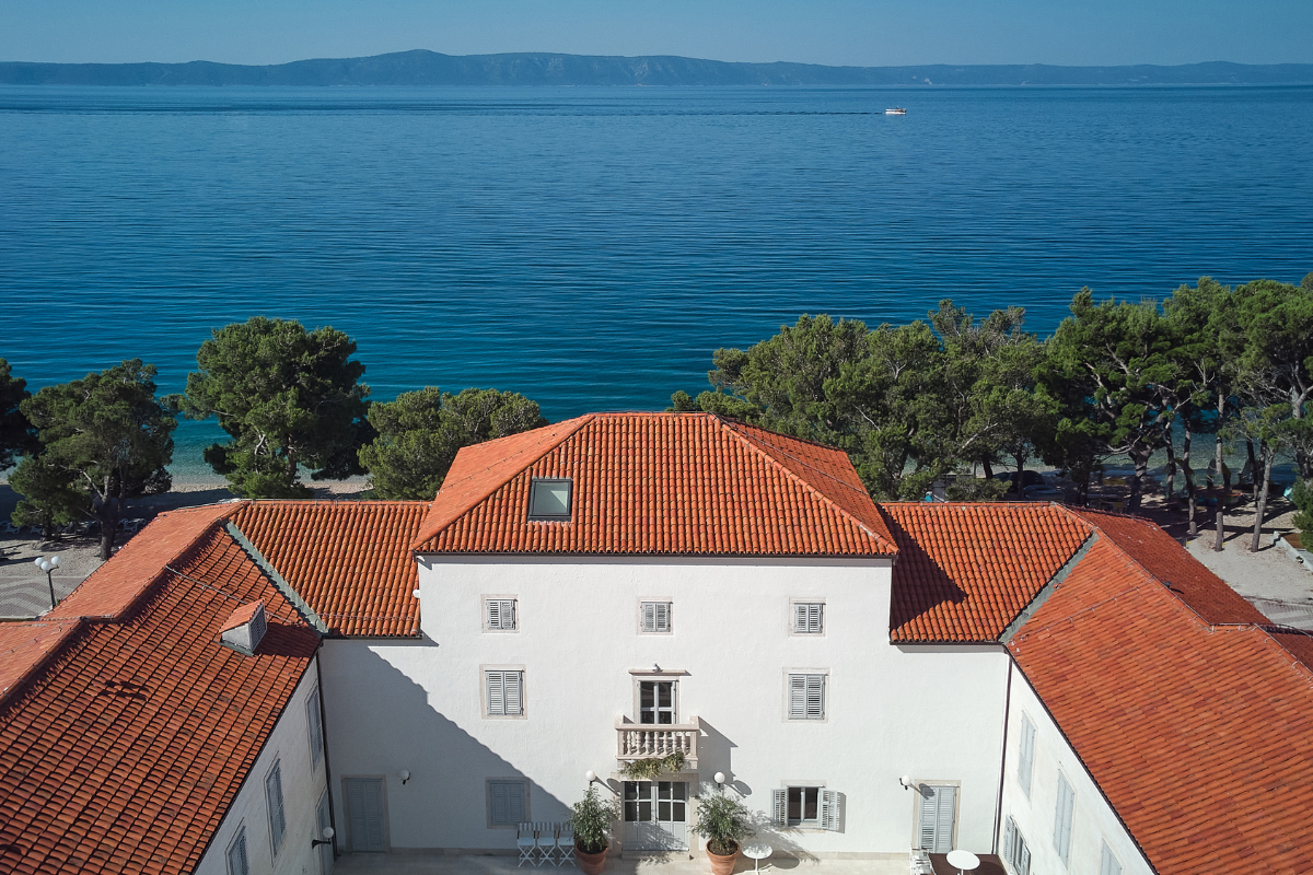 a building with a red roof and trees and a body of water