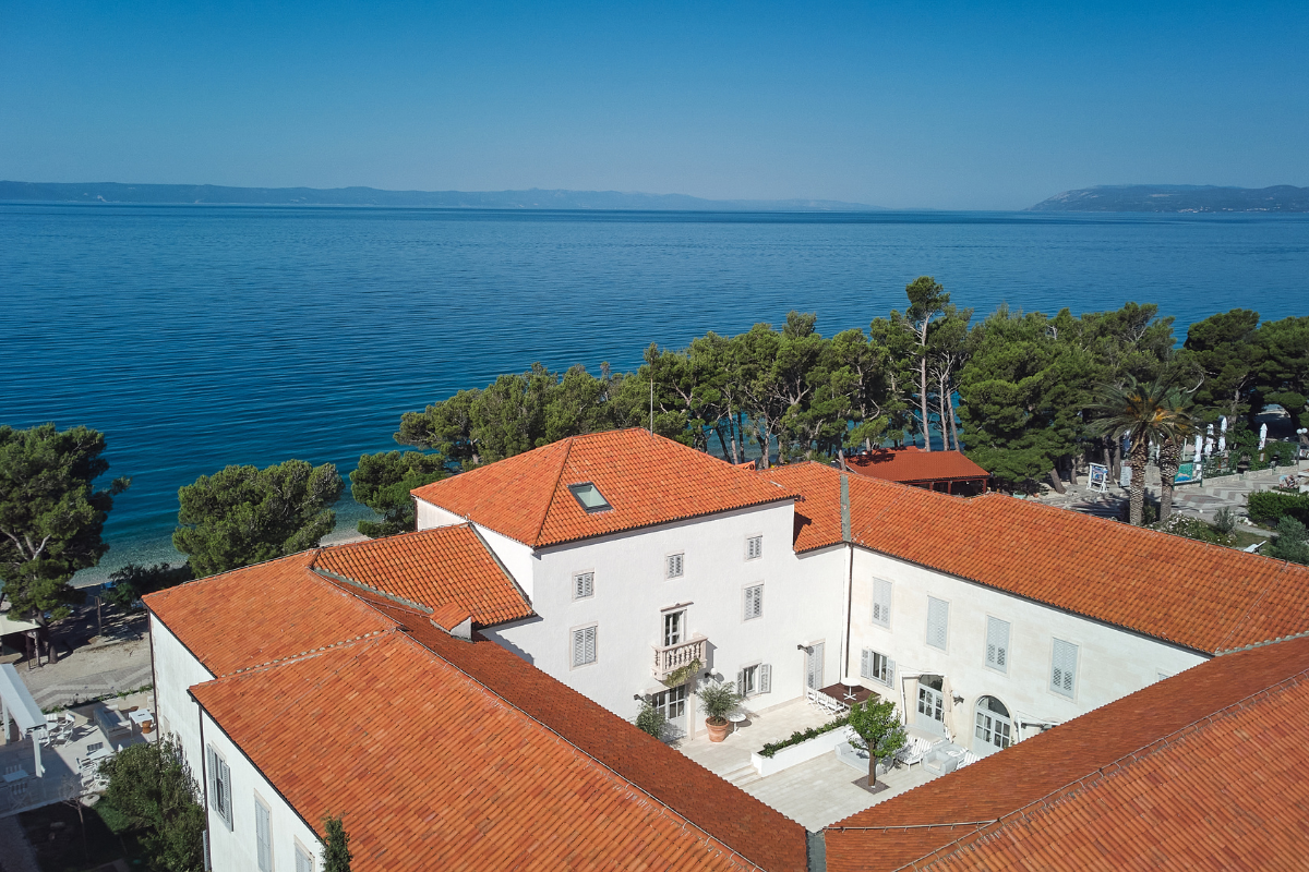 a large white building with orange roofs and trees next to a body of water