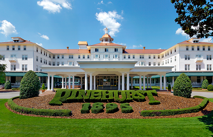 a large white building with columns and a sign in front of it with Pinehurst Resort in the background