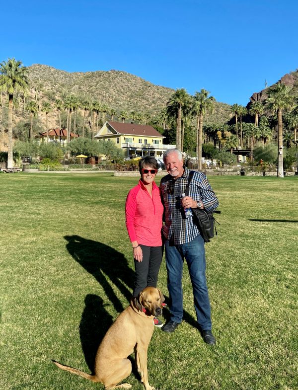 a man and woman standing in a grassy area with a dog
