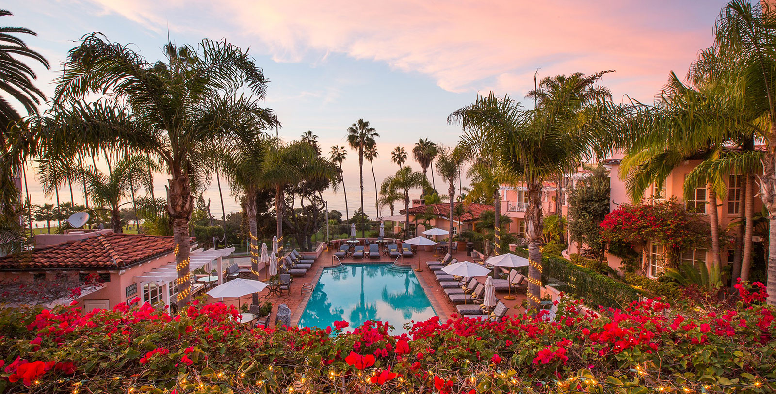 a pool with umbrellas and chairs surrounded by palm trees