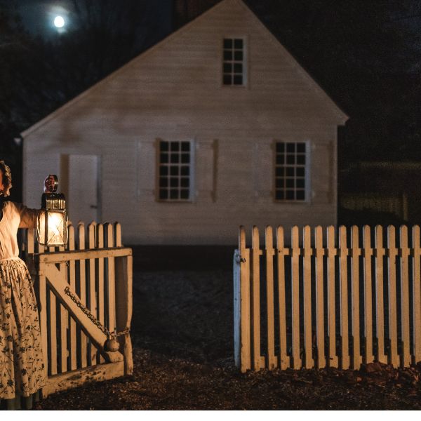 a woman holding a lantern in front of a white fence