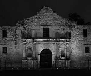 a stone building with a door with Alamo Mission in San Antonio in the background