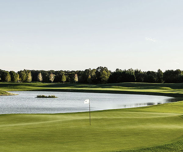 a golf course with a flag on the green with Geneva National Golf Club in the background