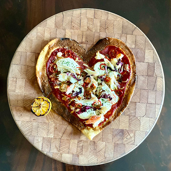 a heart shaped pizza on a wood plate