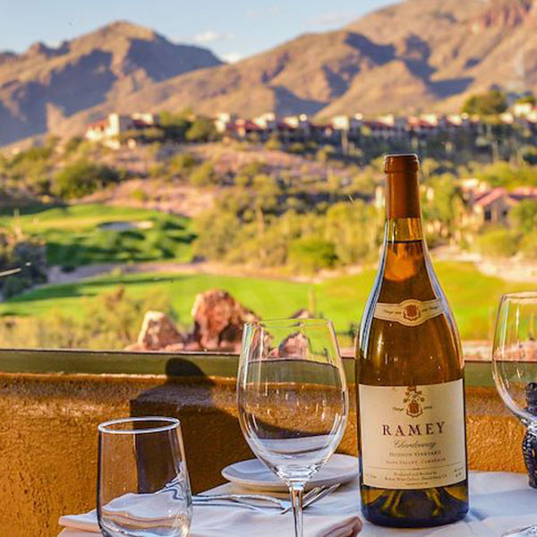 a wine bottle and glasses on a table with a view of mountains and hills