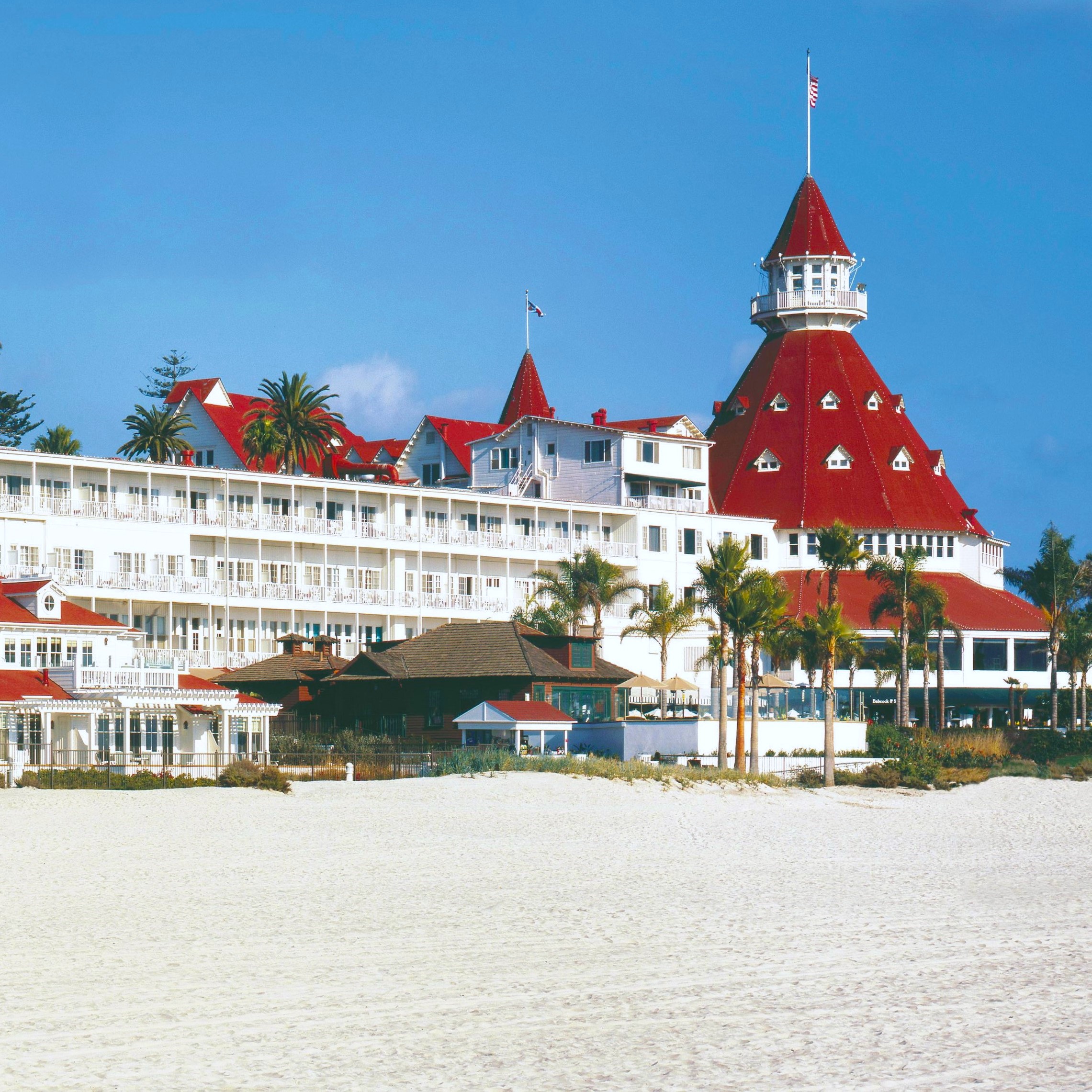 a large white building with red roofs and a tower on the beach