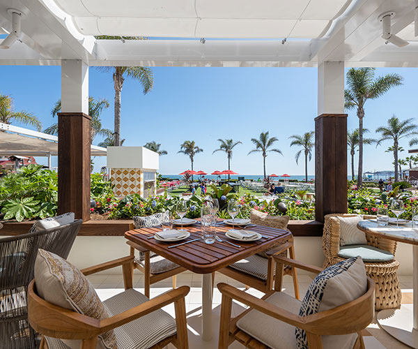 a table and chairs outside with a view of the beach and palm trees