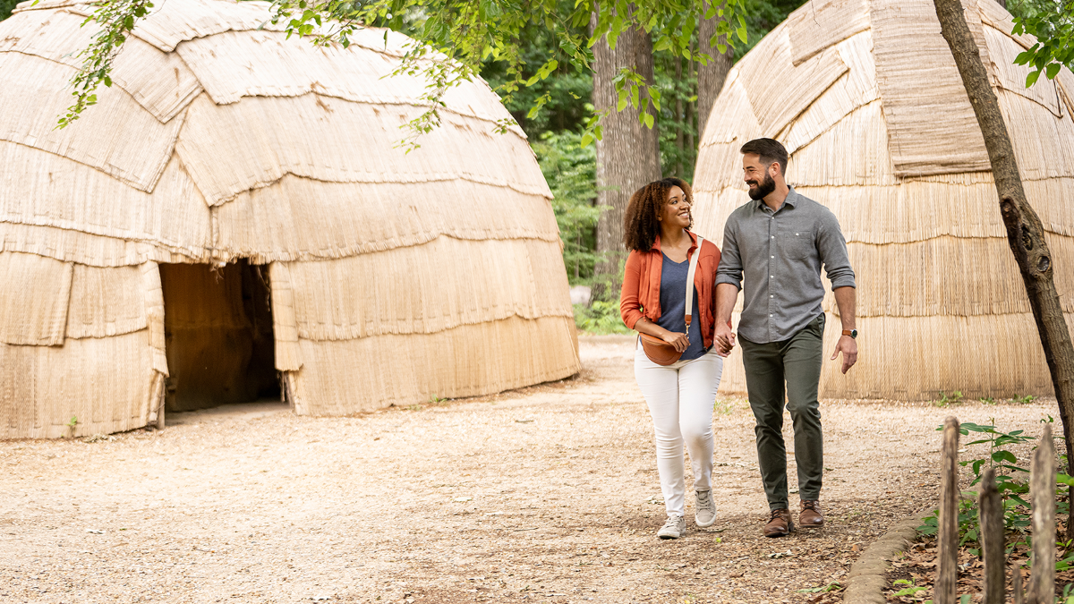 a man and woman holding hands and walking by straw huts