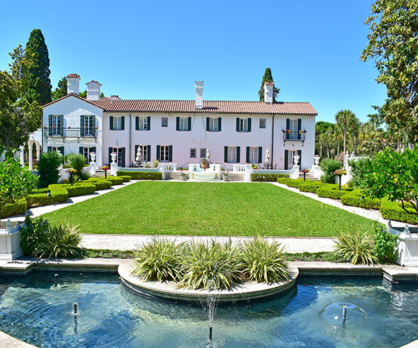 a large white house with a large lawn and fountain with Jekyll Island in the background