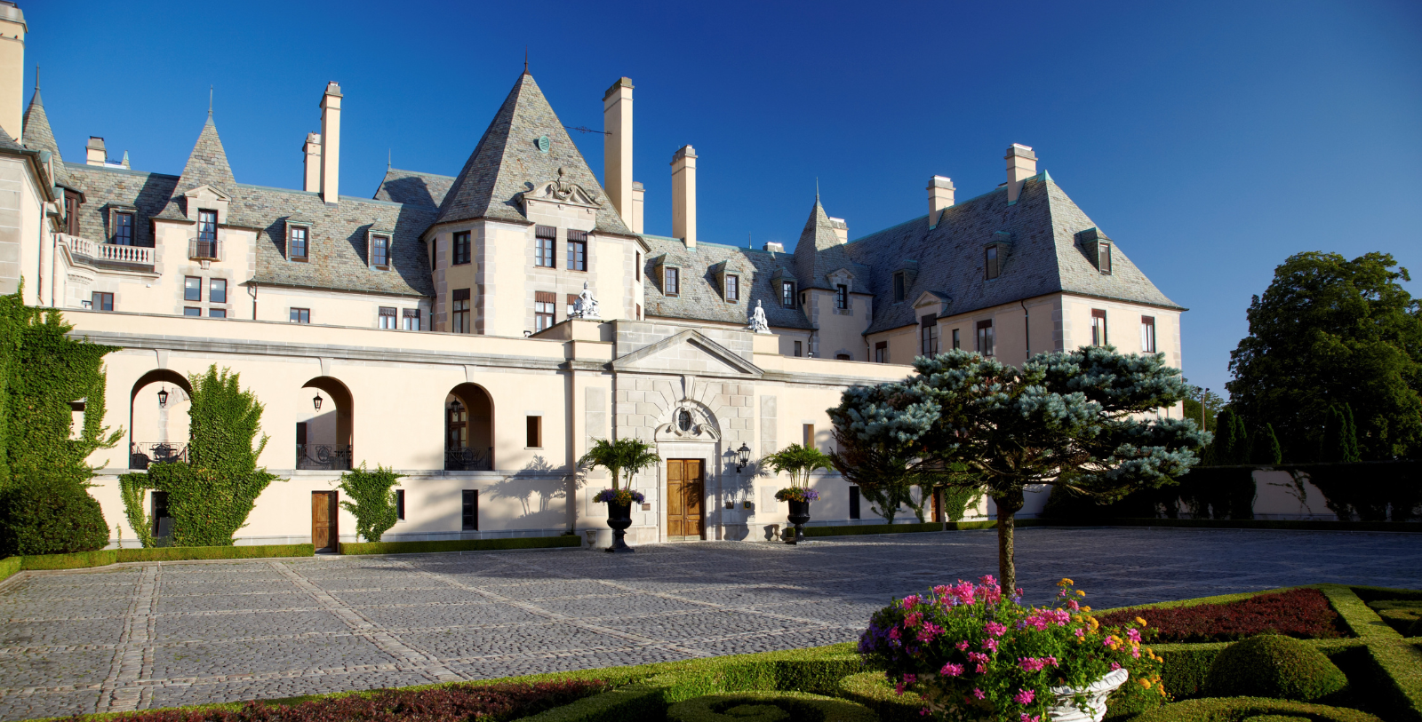 a large white building with a stone driveway and trees