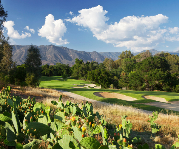 a golf course with cactuses and mountains in the background