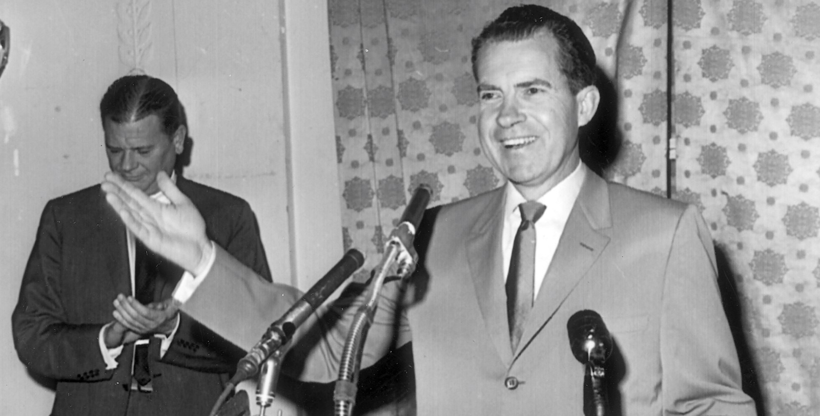 a man in a suit and tie standing in front of microphones