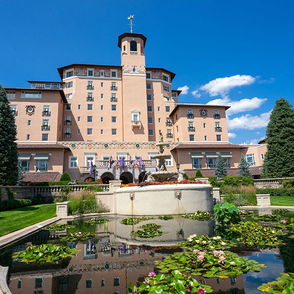 a large building with a fountain and a pond in front of it with The Broadmoor in the background
