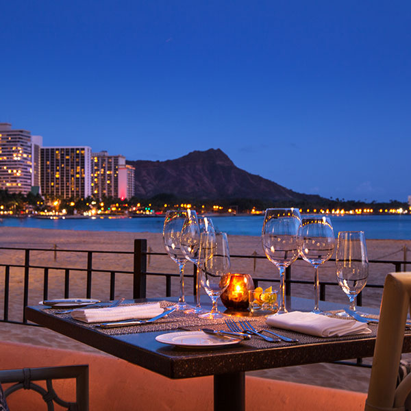 a table with wine glasses and candles on it by a beach